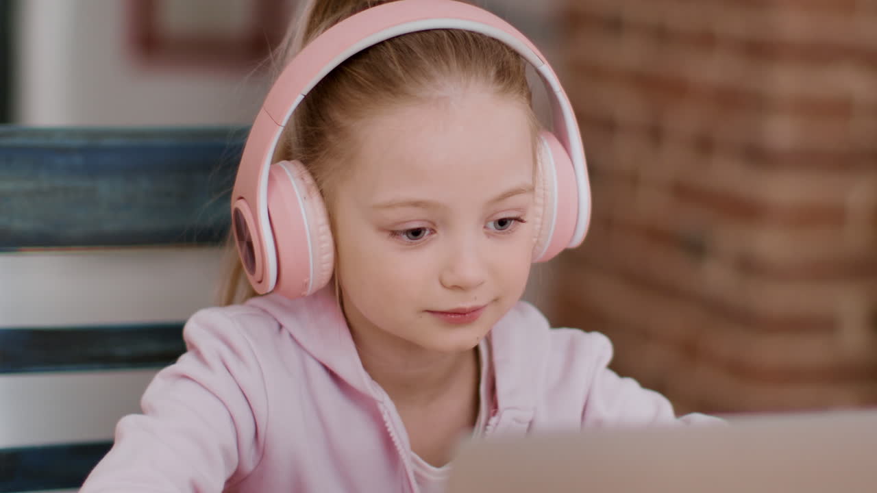 Young Girl with Pink Headphones Using a Laptop