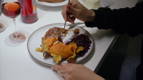 mujer usa el tenedor para comer patata dulce con mantequilla, pato asado, repollo rojo, disfrutando de una comida festiva con vino rojo, dieta saludable y equilibrada, comida casera, cena de navidad, delicioso plato cálido, primer plano