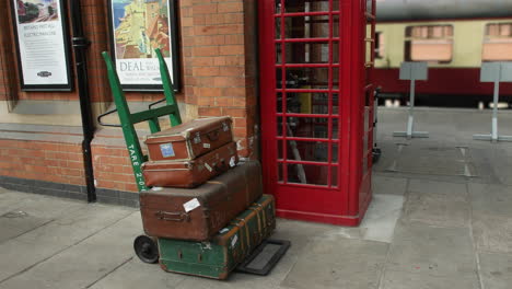 antique vintage luggage suit cases on a trolly on the platform at a train station in england with a red telephone box