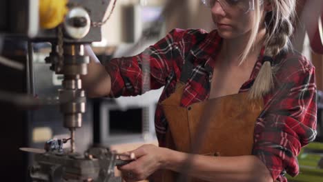 downward tilt, focused blonde woman operates drill press in metal shop