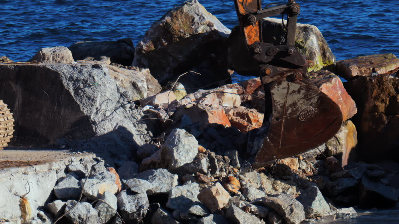 A large, yellow and rusty excavator picking up rocks and water from the sea