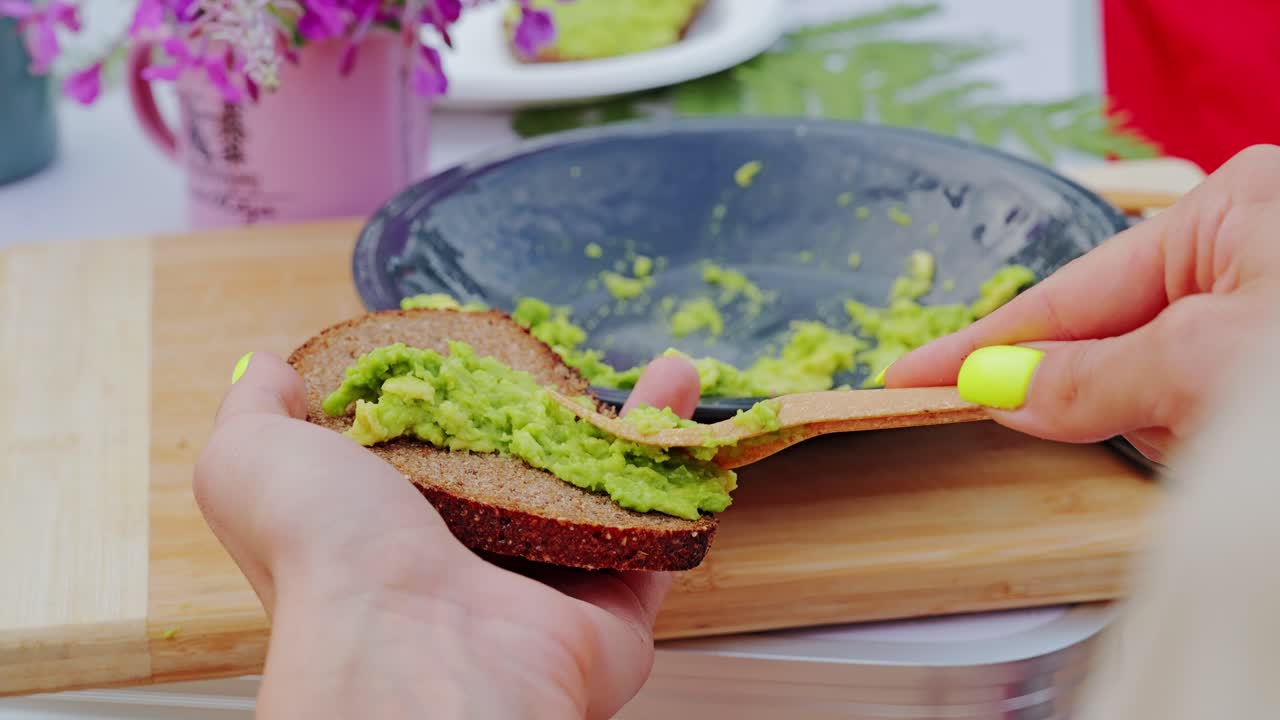 Close up of woman spreading creamy avocado on dark rye bread in slow motion
