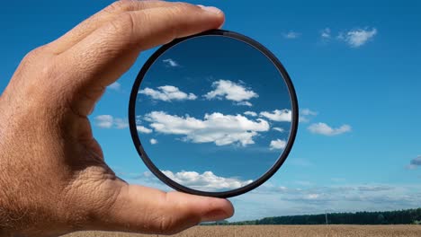 efecto visual del filtro polarizador en el ejemplo de un paisaje rural de verano con hermosas nubes. la mano sostiene un filtro circular, aplicando el efecto de polarización.