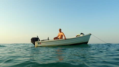 solitary shirtless man on board of small floating anchored rolling motorboat