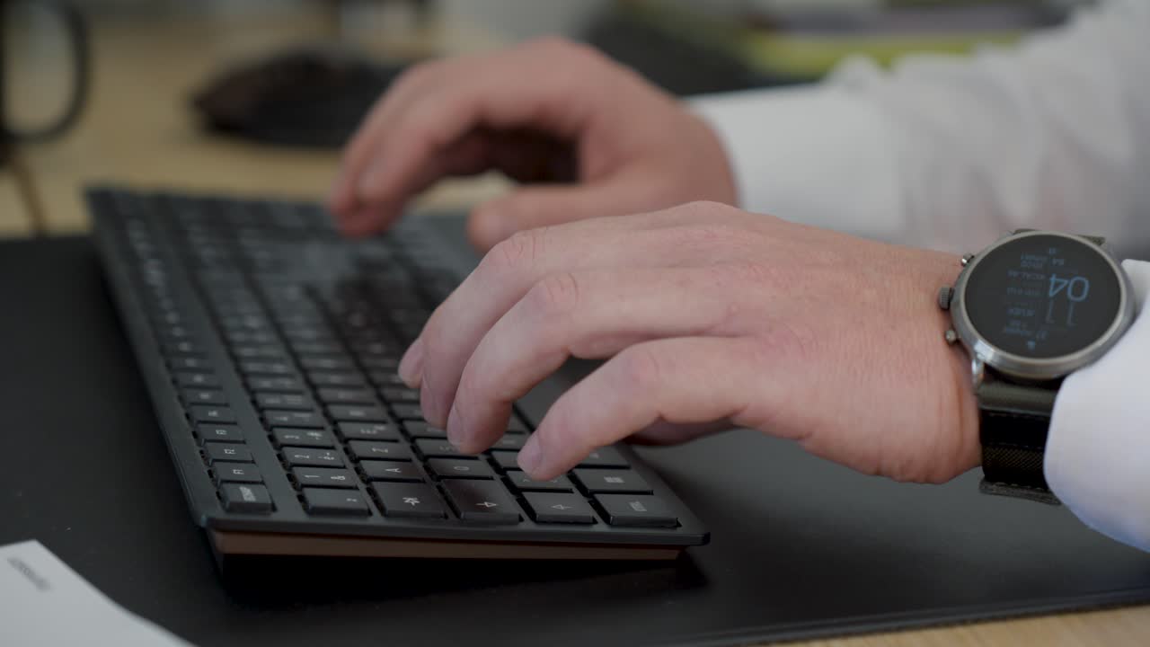 un primer plano de un hombre escribiendo en un teclado con una camisa y un reloj inteligente