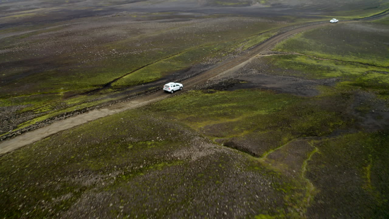 흰색 4x4 자동차가 아이슬란드 고원, 검은 화산, 바위 풍경, 오프로드 흙길을 따라 운전합니다.