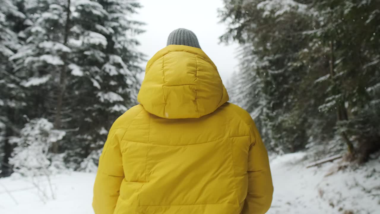 Person in a yellow jacket walking through a snowy forest