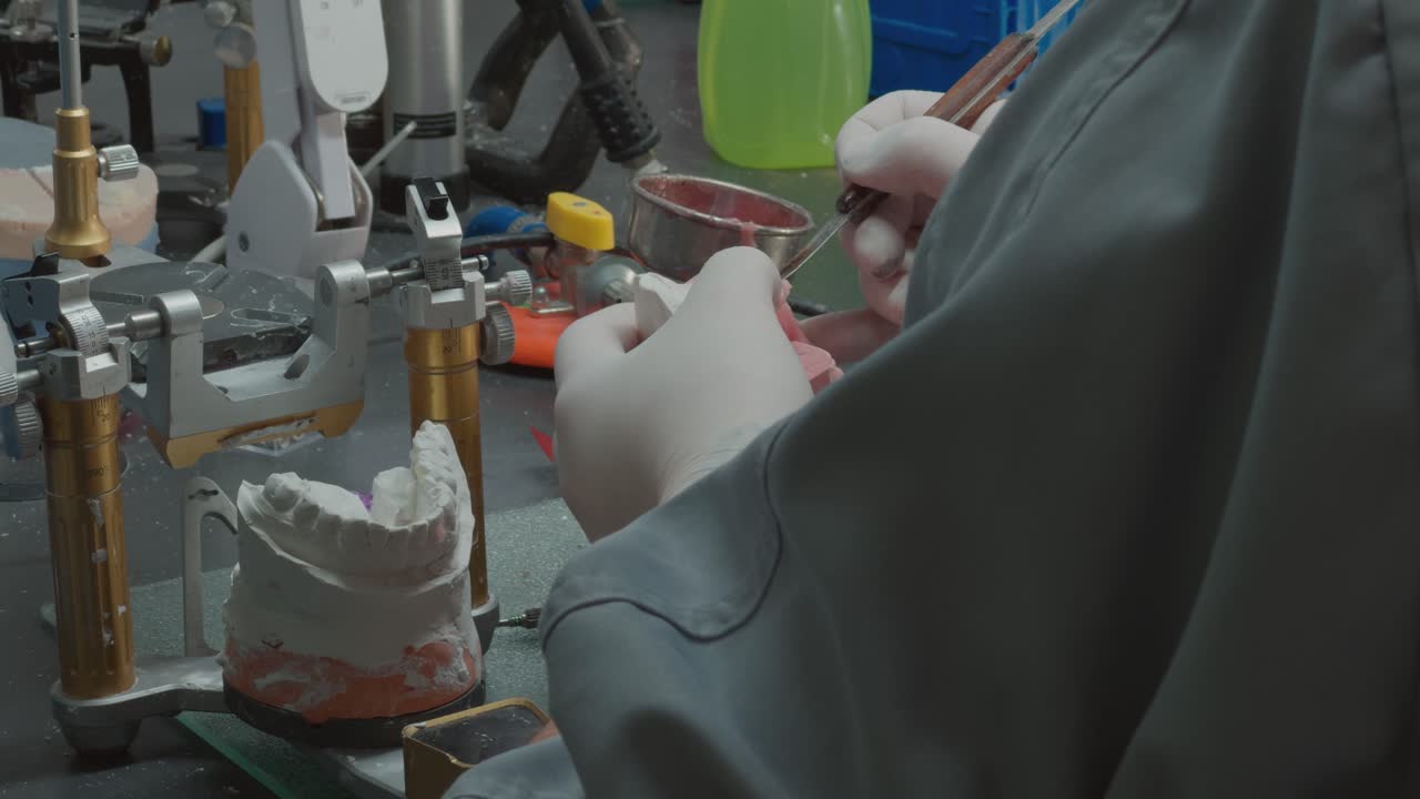 Manos enguantadas dando forma a un molde dental junto a herramientas en una mesa de laboratorio.