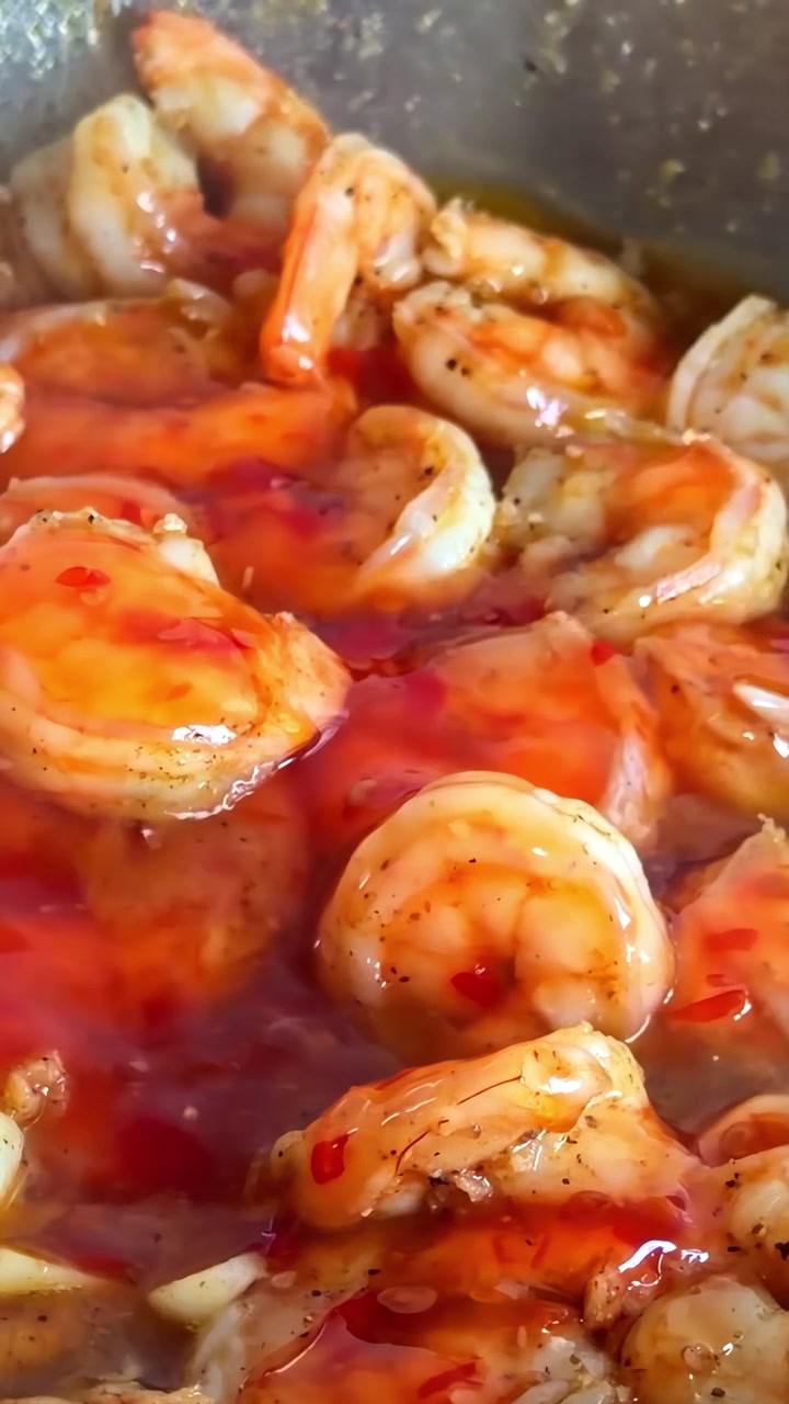 Gamberi succulenti in cottura in una salsa rossa vivace e piccante, che mostra colori e consistenze ricche. Ideale per blog culinari o tutorial di cucina.