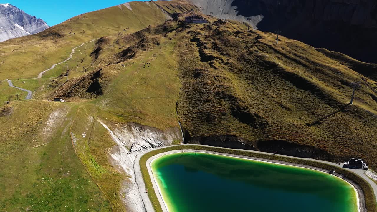 Drone footage of a mountain reservoir surrounded by alpine hills and hiking paths. Scenic aerial landscape in Switzerland, concept for nature, water, tourism, and environment