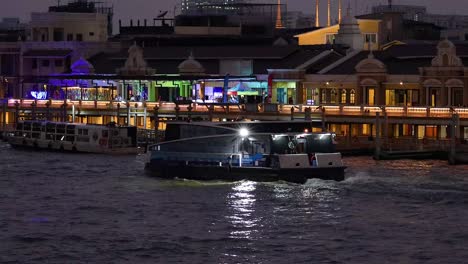 boat travels past illuminated riverside buildings at night