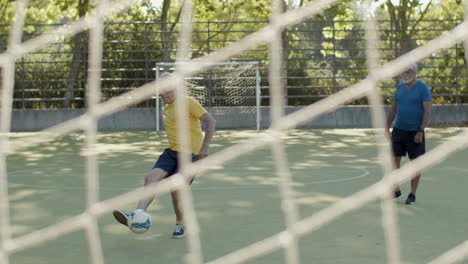 front view of happy senior man kicking ball, scoring a goal and celebrating while playing footbal with friends in a stadium