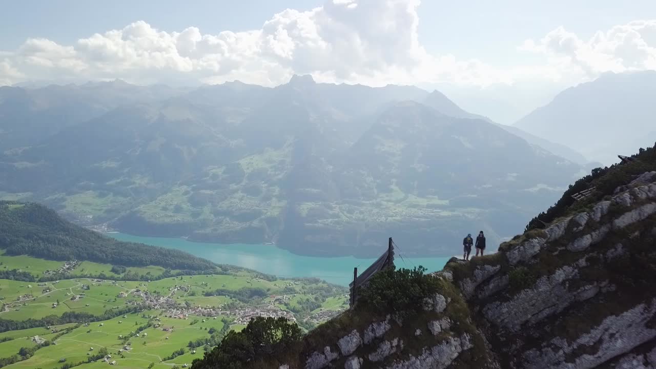 drone vuela desde una vista increíble hacia atrás sobre una pequeña cresta de montaña donde dos personas están de pie sobre ella