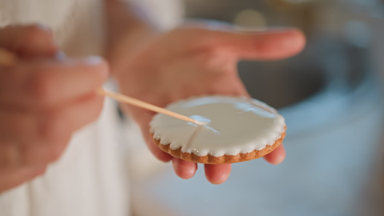 Pumpkin cookie iced with glaze, hand using skewer to spread smooth white icing over scalloped edge, artisan baker detail shot, careful steady motion, pastry workshop and home decorator scenes