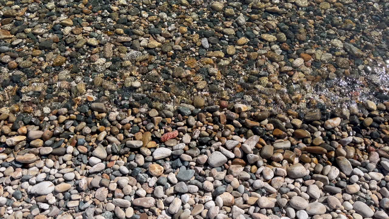 Soothing view of small waves flowing over beach pebbles at Fokos Beach at Greece's Mykonos Island. Perfect for travel, nature, peaceful, or meditation video content