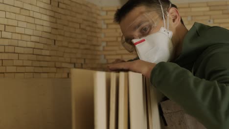 trabajador de la madera profesional en máscara y gafas comprueba la madera en bruto, tabla de madera, panel de contrachapado