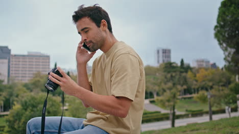 viajero alegre hablando por teléfono móvil mirando fotos en la cámara en el parque de primer plano