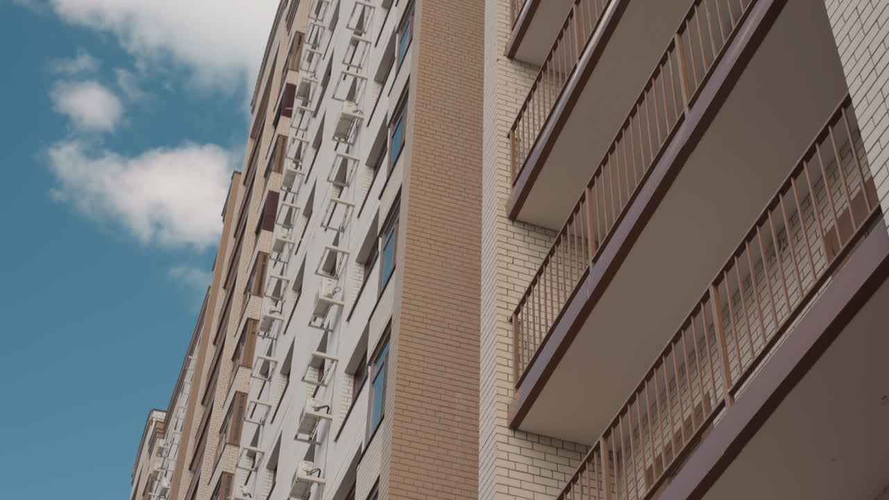 낮은 앵글에서 보이는 다층 주거용 건물과 금속 파고라, 격자를 타고 올라가 철제 막대에 매달린 녹색 덩굴, 건축 세부 사항과 벽돌 텍스처가 프레임을 지배하고 있어요.