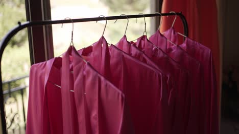 set of bright pink bridesmaid robes hanging neatly on a garment rack, ready for the wedding day