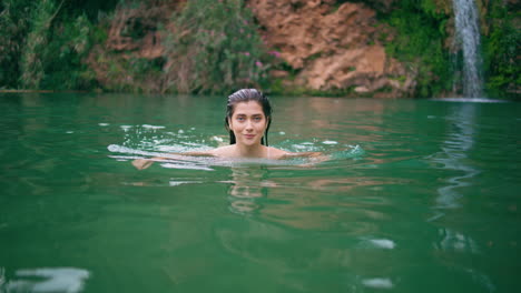 modelo desnudo nadando en el lago del acantilado en la hermosa naturaleza de verano. mujer mirando cámara