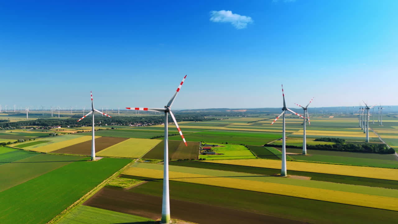 Geometrical agricultural fields away from the big cities. Wind turbines rotate slowly in the wind.