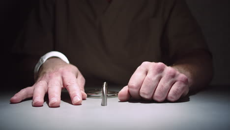 close-up das mãos de um prisioneiro enquanto ele se senta calmamente algemado a uma mesa em uma sala de interrogatório