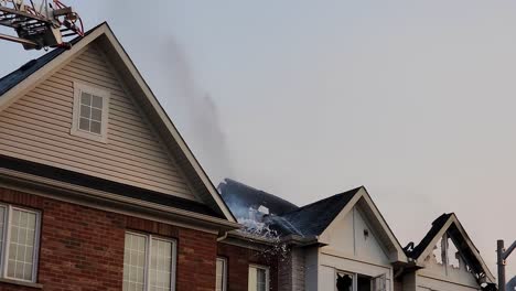 Fire-fighters-spray-water-as-steam-rises-off-of-burnt-charred-house-roof,-static