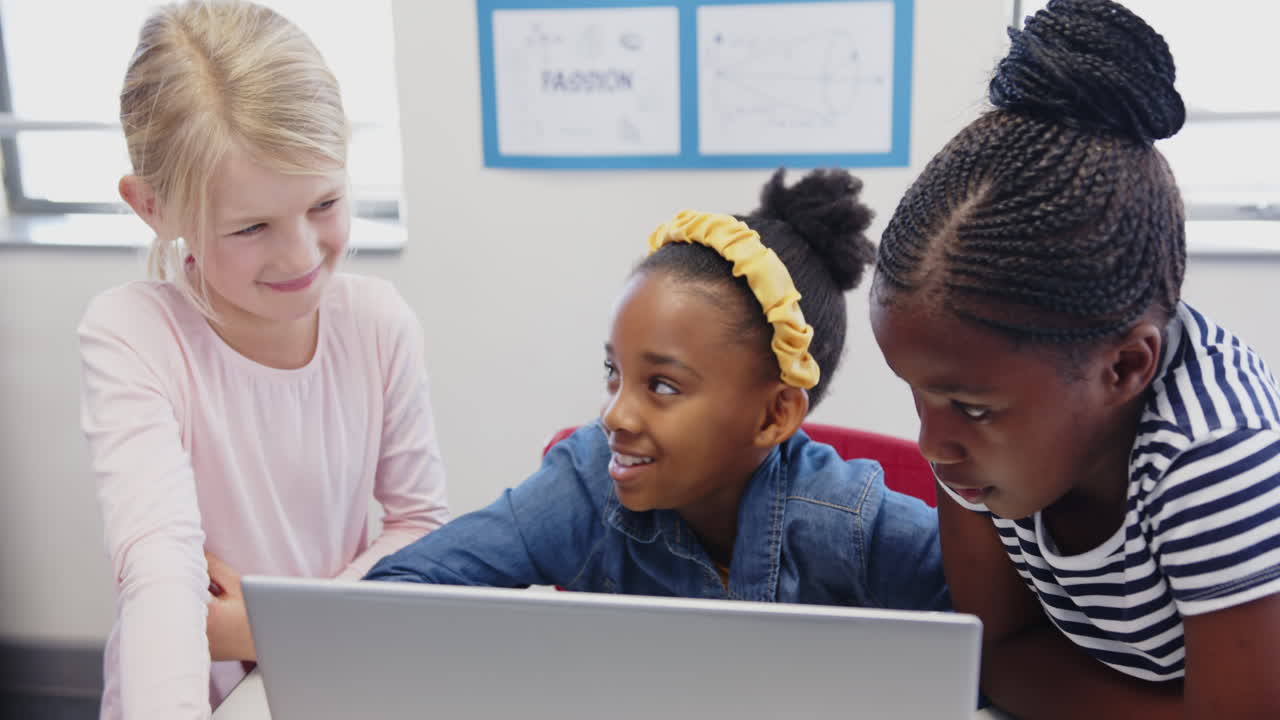 In school, three girls using laptop together, collaborating on project