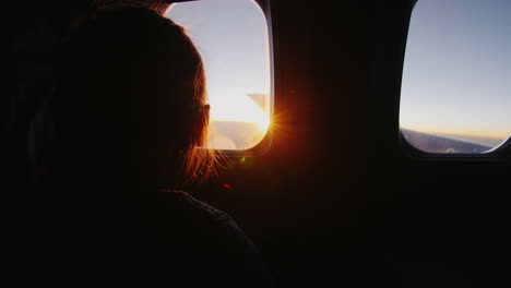 little girl sitting on the plane with delight looks out the window at the rising sun