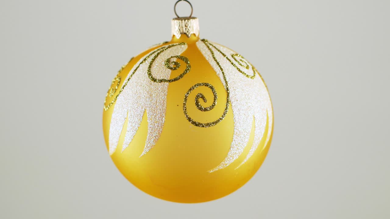 Golden Christmas ball toy turning round and back in luminous light on dark green background. New Year pattern.