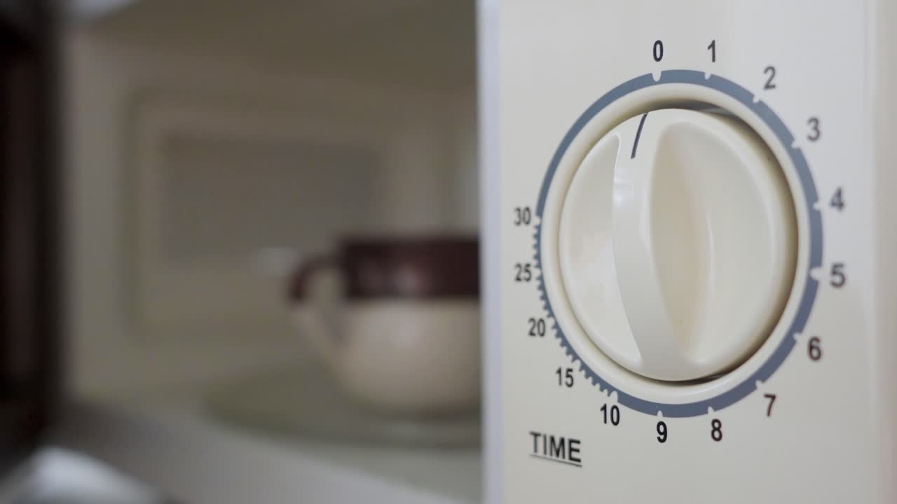 hombre poniendo una taza de café en un horno de microondas y encendiéndolo