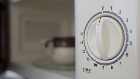 man putting a coffee cup into a microwave oven and turning it on