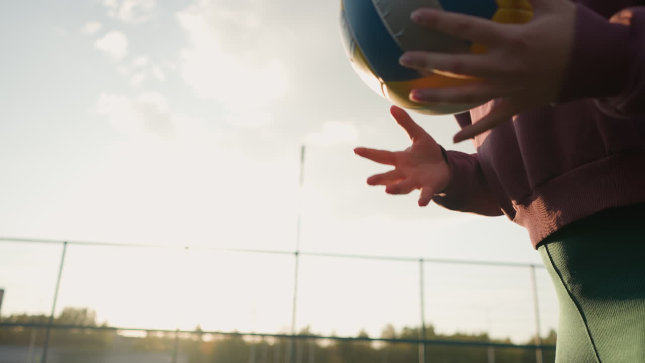 vista parcial en primer plano de una mujer rebotando un balonmano con el brillo de la luz solar en el fondo, creando un efecto vibrante con la vegetación, mostrando deportes al aire libre y un estilo de vida saludable