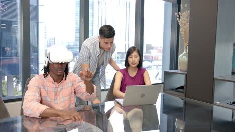 using vr headset, man collaborating with colleagues working on laptop in office