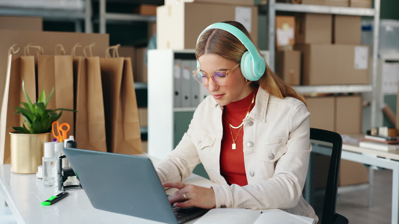 Woman working on laptop with headphones in an office warehouse