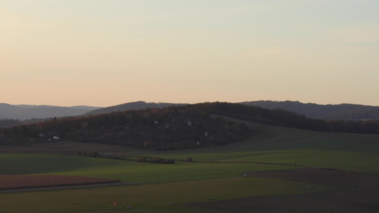 브르노 체코 공화국의 화창한 가을 일몰 지역에서 포착된 산등성이 아래에 지어진 여러 개의 작은 집들을 볼 수 있는 자연 공항 필드와 언덕의 시간 경과