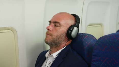 cerca de un hombre relajándose escuchando música con auriculares viajando en un avión de una aerolínea de pasajeros