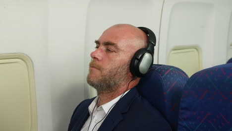 close up of a man relaxing listening to music wearing headphones traveling on a passenger airline plane