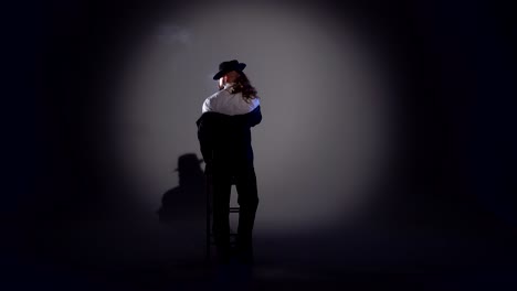 man in suit and fedora under spotlight with chair