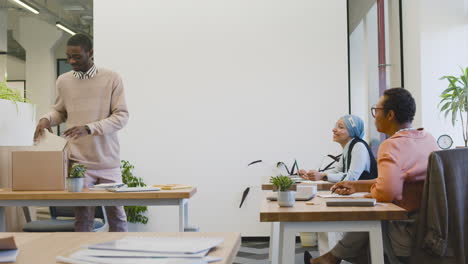 muslim woman and sitting at a table in the office, while a young man takes out his personal items from a box and places them on the table