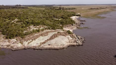 aerial orbit shot of couple walking over rocks on black lagoon in punta del diablo,uruguay