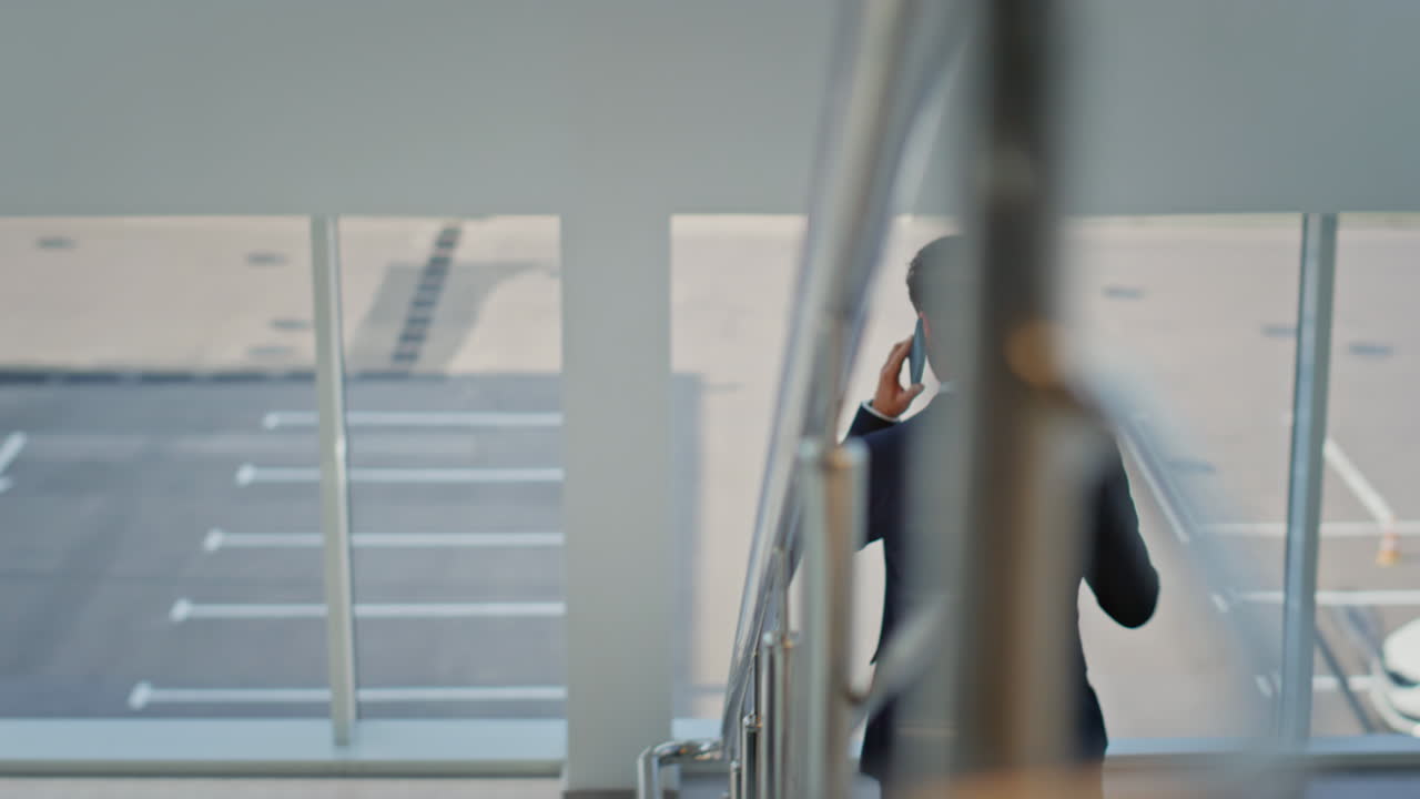 Busy entrepreneur talking mobile phone walking down staircase modern building