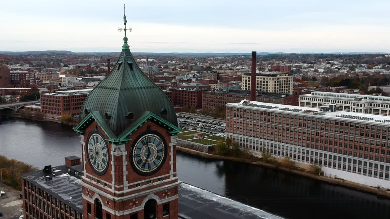 Torre dell'orologio dell'Ayer Mill a Lawrence, Massachusetts, che si affaccia sul fiume Merrimack e sul ponte di giorno - ripresa aerea ravvicinata, in orbita