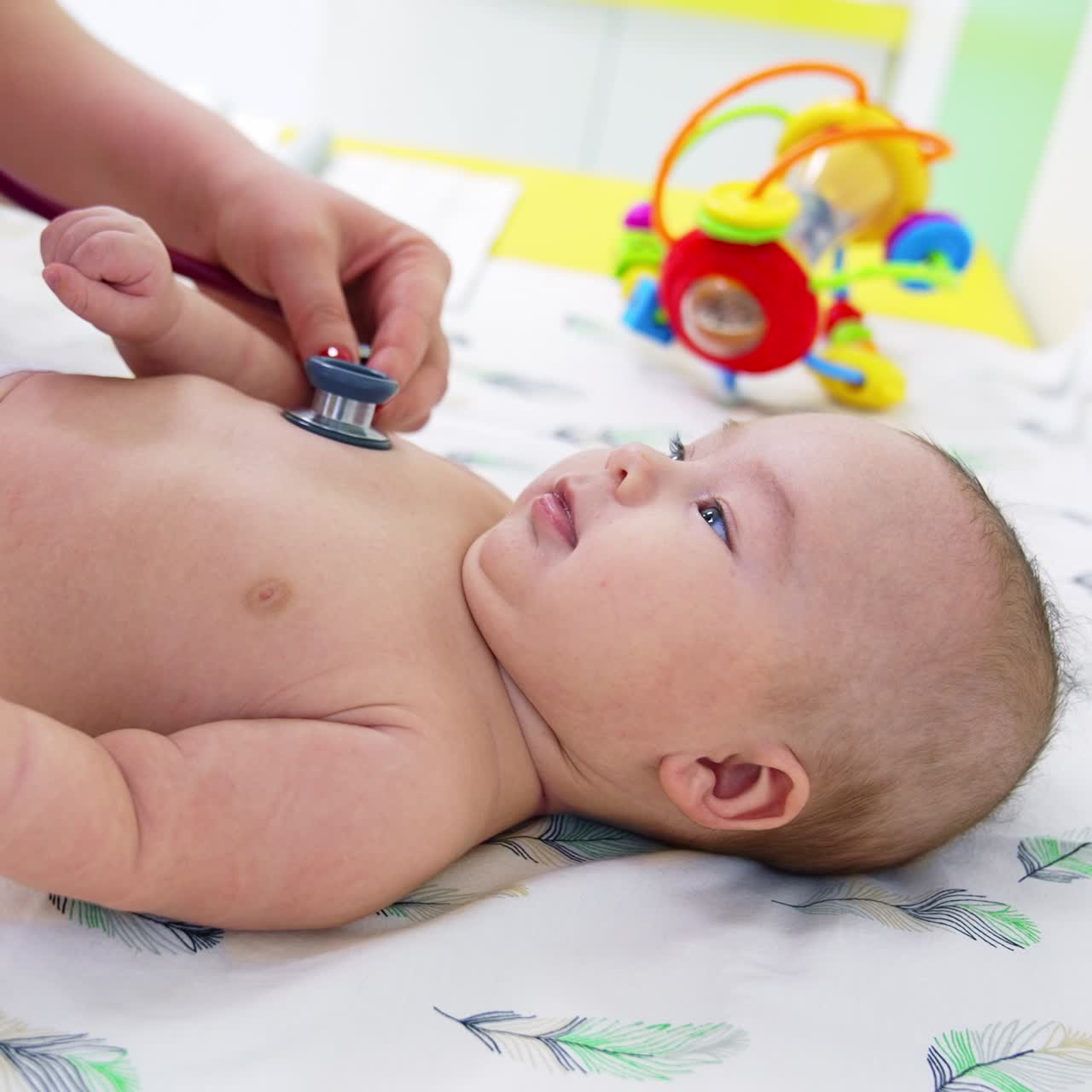 Pediatrician putting stethoscope to little boy's chest. Doctor distracting baby's attention by showing a colorful toy. Close up
