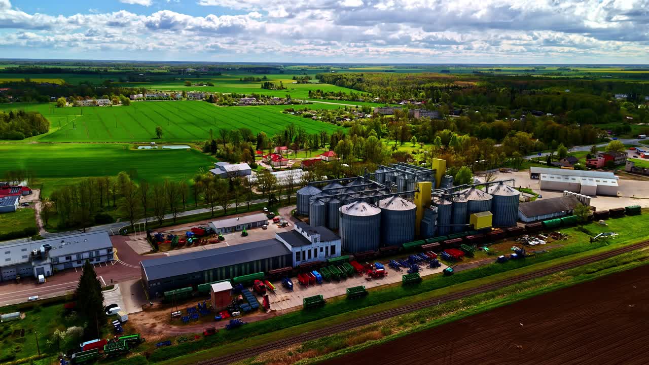 Luftaufnahme einer riesigen Industrieanlage mit Silos und Lagerbereichen inmitten von Feldern und Wiesen.