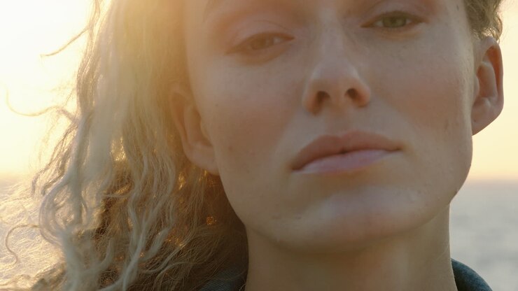close up portrait of beautiful blonde woman looking confident enjoying relaxed vacation lifestyle feeling freedom on seaside at sunset