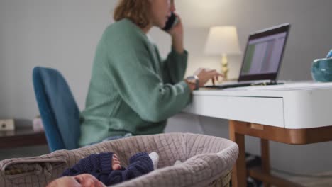 Video-of-caucasian-mother-working-on-laptop-from-home-with-newborn-baby