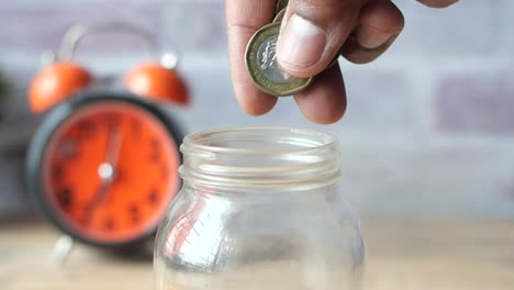 una persona guardando monedas en un frasco de vidrio