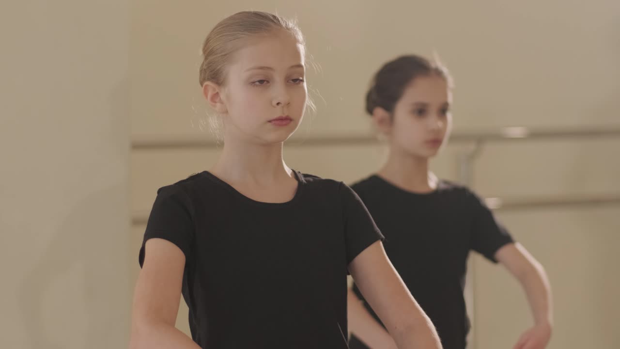 группа молодых студентов балета в черной танцевальной одежде практикует позиции в просторной балетной студии с деревянным полом и настенными решетками. сосредоточенные выражения и синхронизированные движения.