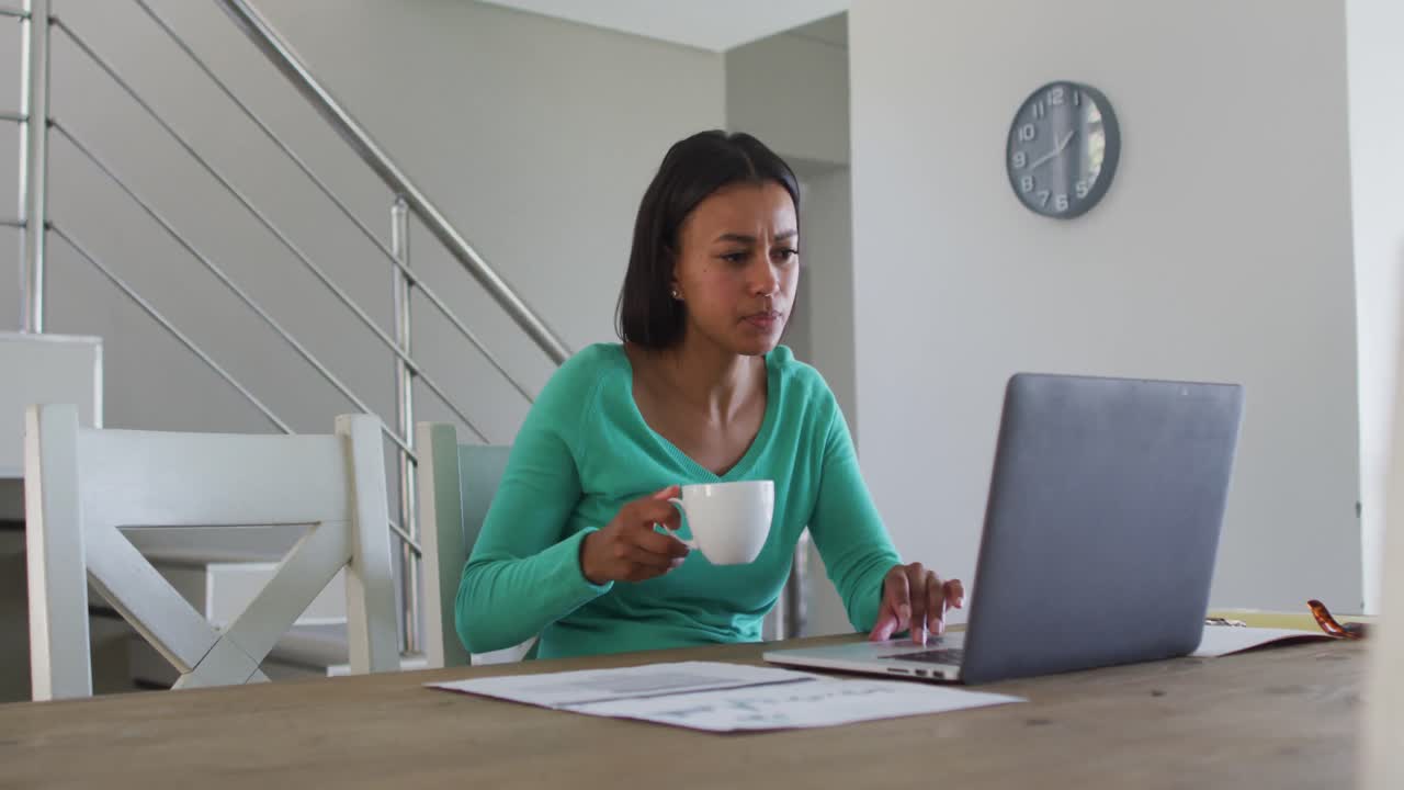 African american woman drinking coffee and using laptop while working from home